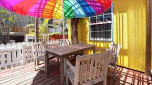 Une terrasse extérieure avec des meubles en bois, un parasol coloré et un mur jaune.