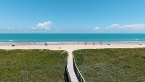 Een strand met een houten promenade die naar de kust leidt, een heldere blauwe lucht en een rustige zee.
