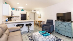 Un espacio habitable compacto con kitchenette, comedor, sofá, televisor y cómoda azul.