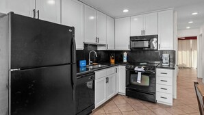 A modern kitchen with white cabinets, a black refrigerator, a microwave, a stove, and a sink. - Relax in Coastal 2-Bedroom Beachfront Comfort (South Padre Island)