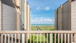 A view from a balcony with a wooden railing, overlooking a beach with a clear sky and ocean. - Relax in Coastal 2-Bedroom Beachfront Comfort (South Padre Island)
