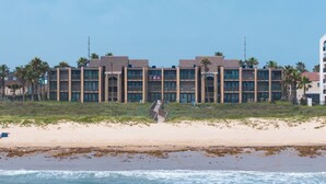 Un hotel frente al mar con varios pisos, balcones y una playa arenosa al frente.