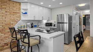 Una cocina moderna con armarios blancos, electrodomésticos de acero inoxidable y una pared de ladrillo decorativa.