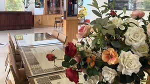 Eine großzügige Lobby mit Holzbalkendecke und einer großen Kristallleuchtre, einem Empfangsbereich und einem Essbereich mit Glastisch.