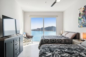 A bedroom with a large bed, a television, a chair, and a view of the sea. - Beautiful Long stay Unit with Premium Ameneties (Mazatlan)