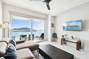A modern living room with a sofa, a coffee table, a TV, and a glass table with a chair. - Beautiful Long stay Unit with Premium Ameneties (Mazatlan)