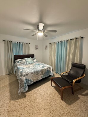 A bedroom with a bed, a chair, a ceiling fan, and curtains.