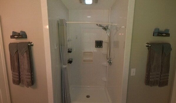 A glass-enclosed shower stall with a handheld showerhead, a towel rack on the left, and a towel rack on the right.