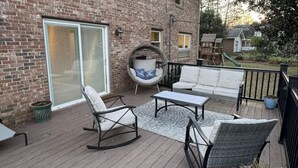 Una terraza de madera con mobiliario exterior, incluyendo una mecedora, un sofá y una mesa.