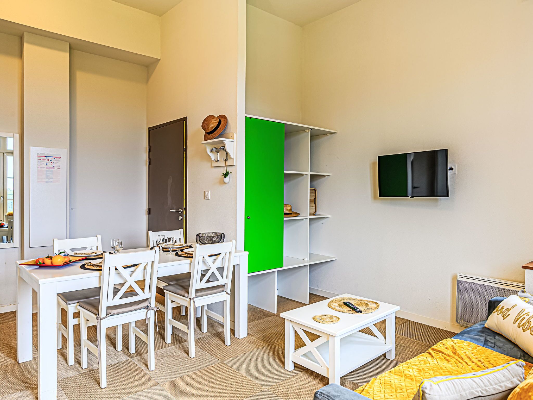 Un espace de vie compact comprenant un coin repas, un séparateur végétal, un téléviseur à écran plat et un canapé agrémenté d’un plaid à motifs.