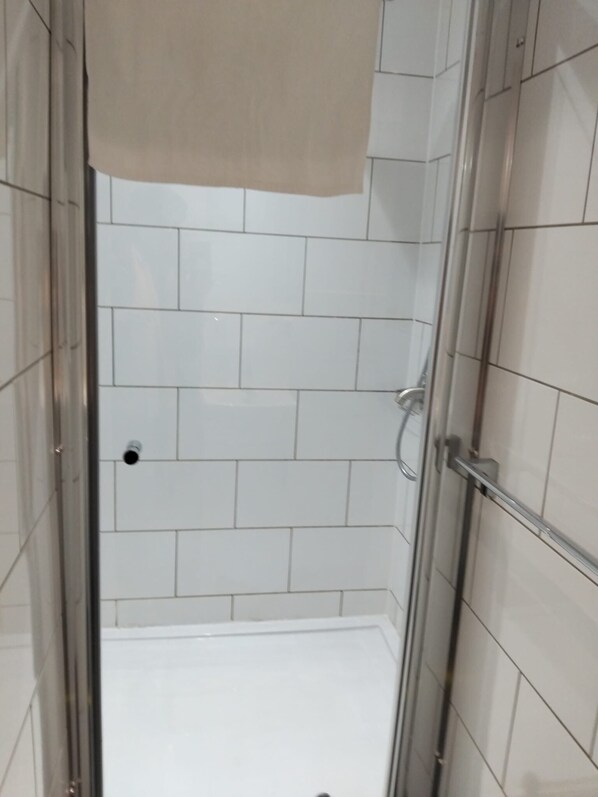 A glass-enclosed shower area with white tiled walls and a metal door.