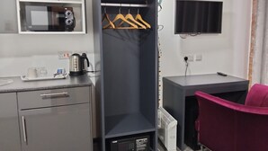 Habitación de hotel compacta con kitchenette, un escritorio pequeño, televisión y armario con perchas.