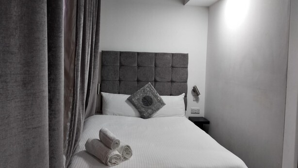 Una habitación de hotel moderna con un cabecero capitonado, una cama bien hecha con sábanas blancas y un par de toallas enrolladas sobre la cama.