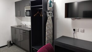 Habitación de hotel compacta con kitchenette, televisor de pantalla plana y armario con perchero.