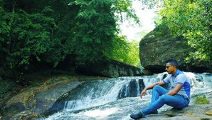 A person sitting on a rock by a waterfall surrounded by dense greenery. - Makeliya Jungle & Waterfall Tour (Kelinkanda)