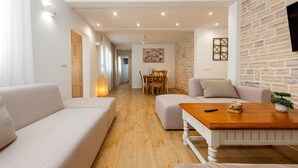 Un salon moderne comprenant un canapé, un pouf et une table basse, un coin repas avec des chaises et une table, ainsi qu’un mur décoratif en pierre.