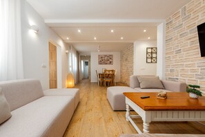 A modern living room with a sofa, ottoman, and coffee table, a dining area with chairs and a table, and a stone accent wall.