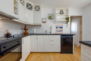 A kitchen with white cabinets, a black dishwasher, and a fruit bowl on the counter.