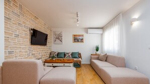 Un salon moderne avec un mur en pierre, un téléviseur à écran plat, un ensemble de canapés, une table basse et une plante en pot.