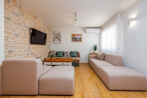 Un salon moderne avec un mur en pierre, un téléviseur à écran plat, un ensemble de canapés, une table basse et une plante en pot.