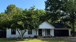 A single-story white house with a black garage door, surrounded by a well-maintained lawn and a large tree to the right.
