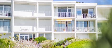 A multi-story hotel with balconies, a covered outdoor seating area, and a garden pathway.
