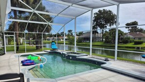 A covered outdoor swimming pool with a hot tub, surrounded by a view of a lake and residential houses.