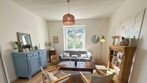 A living room with a sofa, coffee table, chairs, a blue cabinet, a hanging light fixture, and a window with a view.