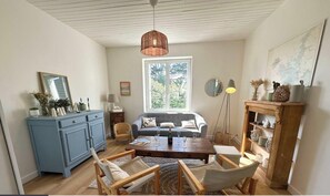 Ein Wohnzimmer mit einer Couch, einem Couchtisch, Sesseln, einem blauen Schrank, einer Pendelleuchte und einem Fenster mit Blick.