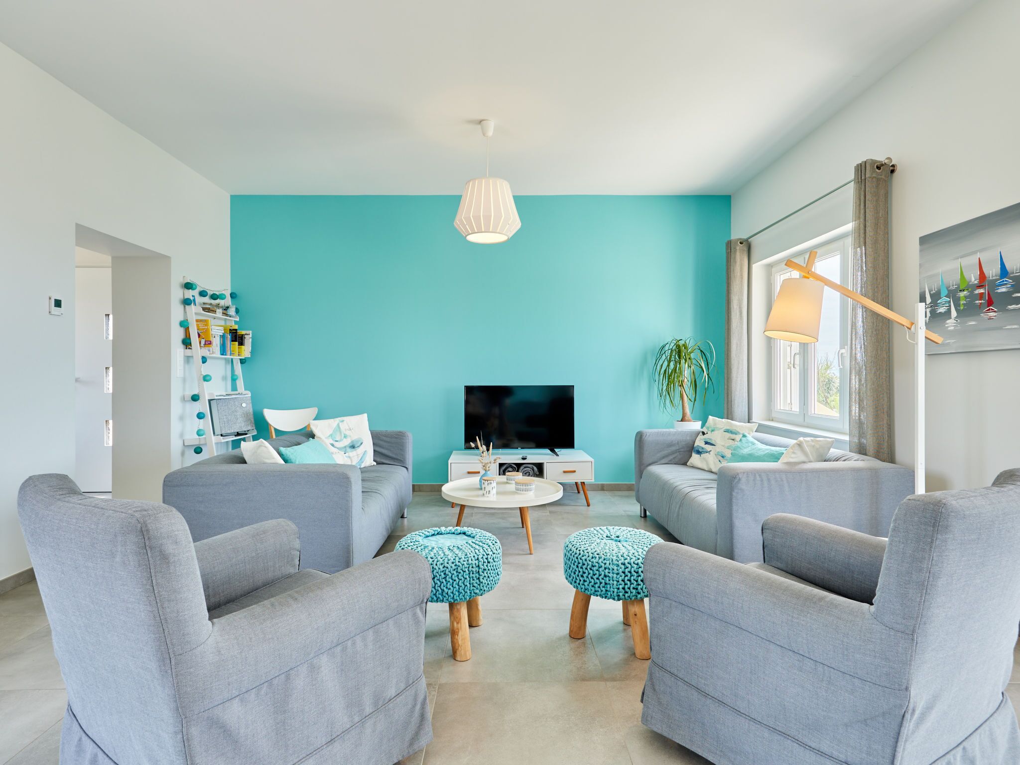 Un salon moderne aux murs de couleur turquoise, avec des canapés gris et une table basse centrale.
