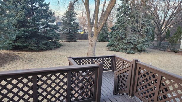 A wooden deck with lattice railings, surrounded by trees and a grassy area.
