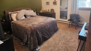 A bedroom with a bed, a nightstand, a dresser, a chair, a window, and a wall with decorative items.