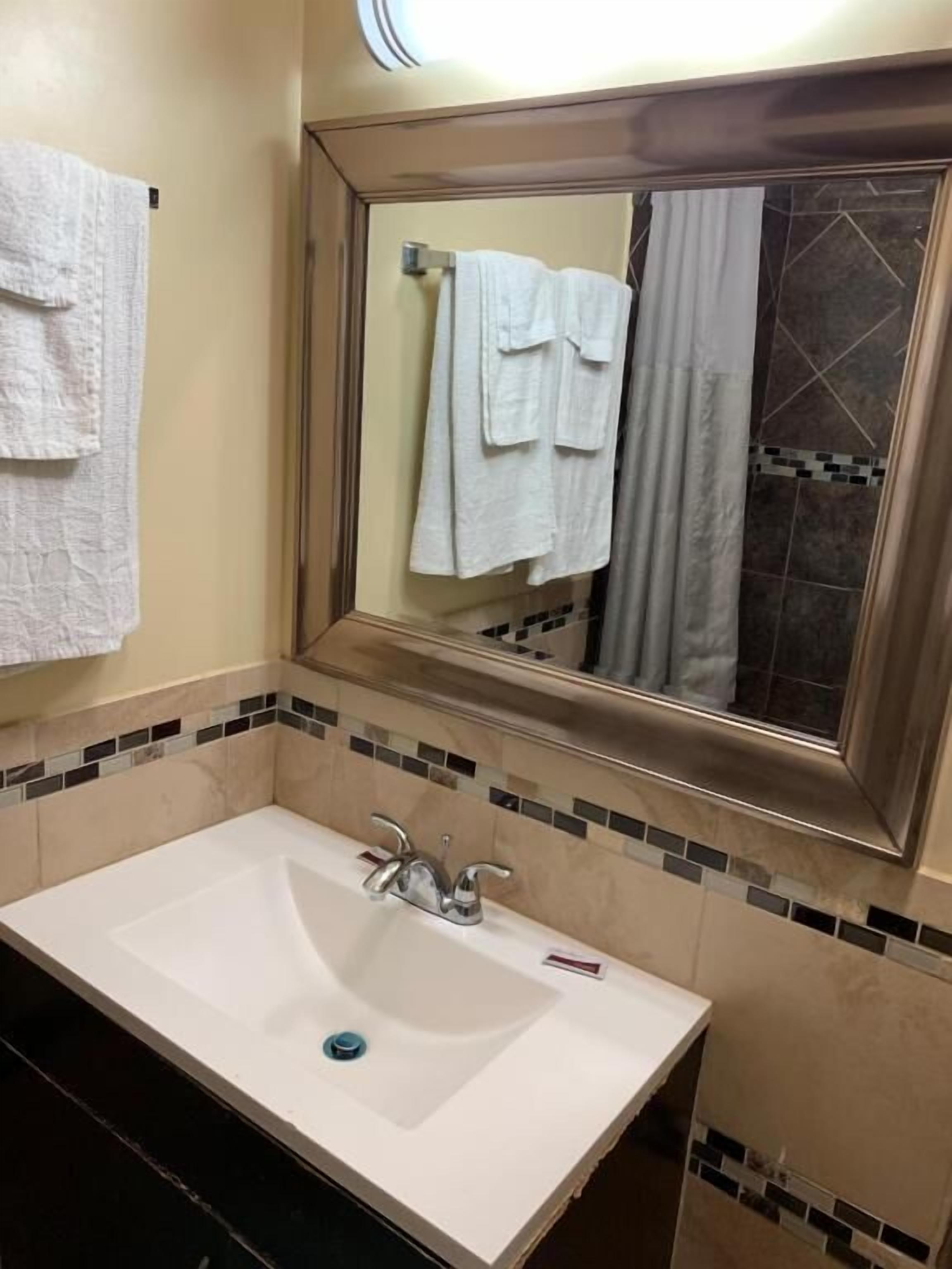 Ein Badezimmer mit einem weißen Waschbecken, einem Spiegel mit Fliesenrahmen und einem Handtuch an der Wand.