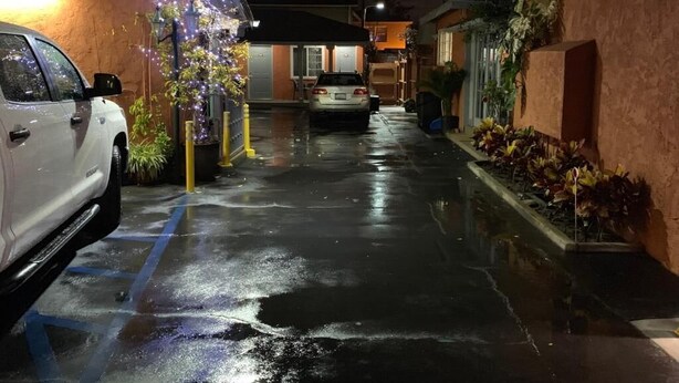 Ett parkeringsgarage med våta golv, en vit bil och en byggnad med en skylt som visar texten ”ANTONIO DR.”.