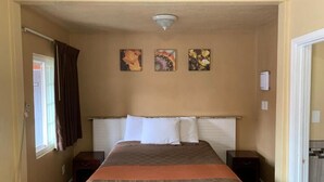 Ett hotellrum med en säng, två sängbord, ett fönster med gardiner och tre konstverk som hänger på väggen.