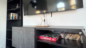 Una sala de estar moderna con un televisor de pantalla plana grande montado en la pared, una estantería empotrada y una mesa de centro con juegos de mesa.