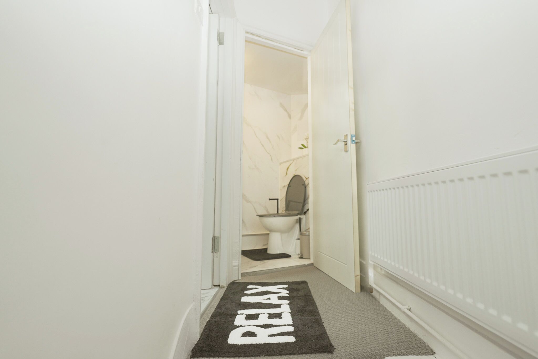 Un couloir menant à une salle de bain équipée de toilettes, d’un bidet et d’un radiateur.