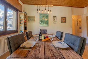 Comedor con mesa de madera dispuesta para seis personas, rodeada de sillas de cuero, y vista a montañas nevadas a través de una ventana.