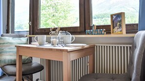 A cozy room with a wooden table set for tea, a window with a view of green trees and mountains, and a radiator.