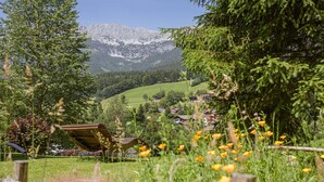 A rural landscape with a mountain range in the background, a small village with houses, and a wooden structure in the foreground.