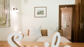 Ett hotellrum med en säng, en inramad tavla på väggen, en dusch och ett träbord med ordet ”Le” skrivet på det.