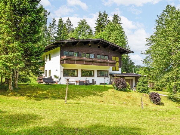 A two-story chalet with a balcony, surrounded by lush greenery and trees. - Studio Esche 2 by Interhome (Ellmau)