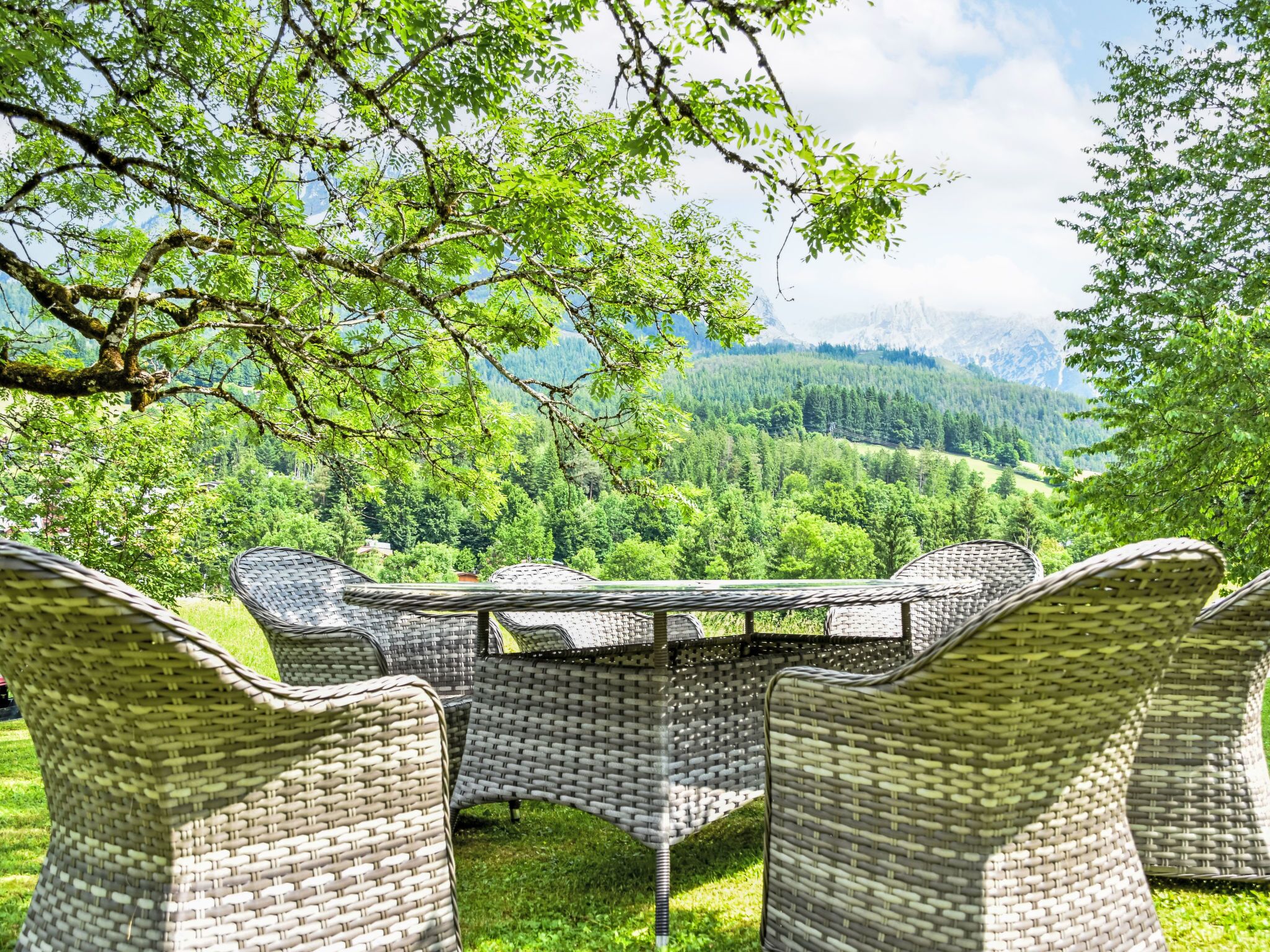 Des meubles en osier disposés autour d’une table, offrant une vue sur un paysage montagneux.