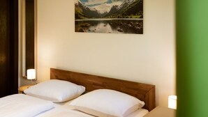 Habitación de hotel con cabecera de madera, dos almohadas blancas y un cuadro enmarcados que muestra un paisaje de un lago y montañas.