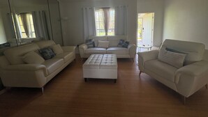 A spacious living room with a large mirror, two white sofas, a tufted ottoman, and a ceiling fan.