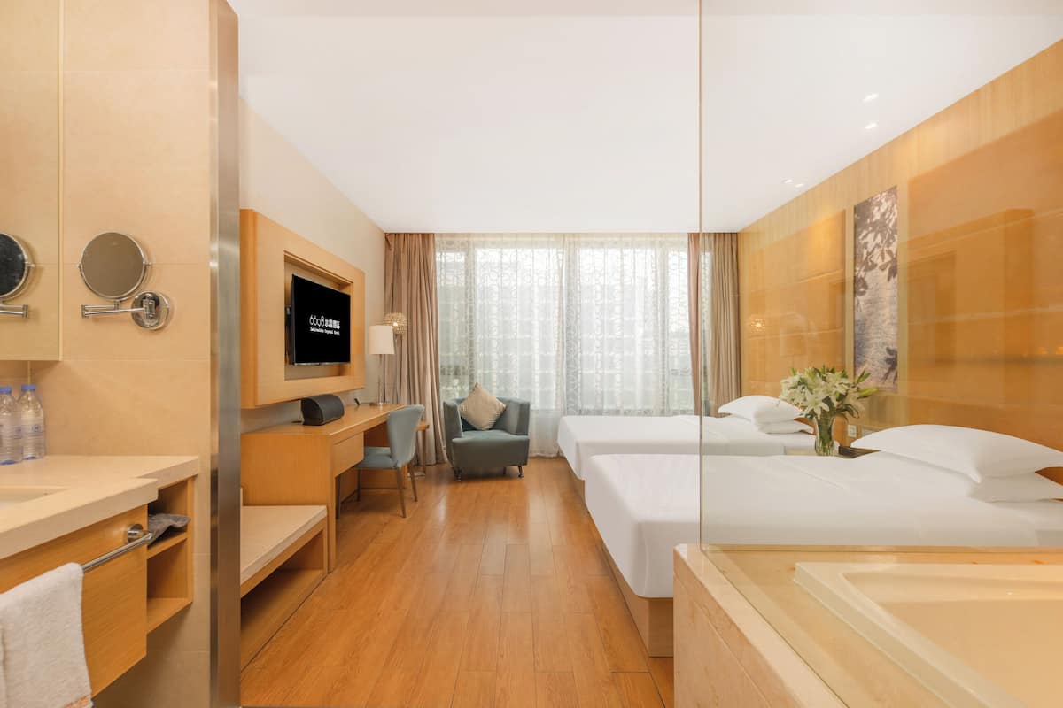 A hotel room with a wooden floor, a desk with a chair, a bed, a TV, and a bathroom with a bathtub.