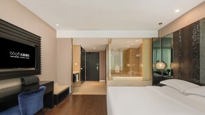 Ein modernes Hotelzimmer mit einem großen Bett, einem Fernseher, einem Schreibtisch und einem Badezimmer mit einer Duschkabine.