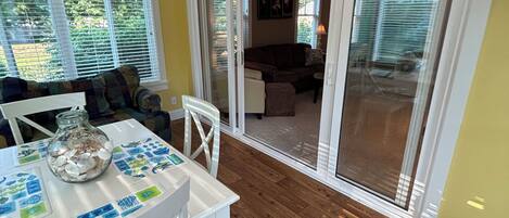 A dining area with a table set for two, a ceiling fan, and a view through a glass door to a living room.