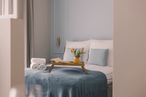 A neatly made bed with a blue blanket, a bedside table with a book and a vase of flowers, and rolled towels on the floor. - Modern Comfort in Nowy Port (Bydgoszcz)