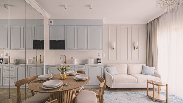 Eine moderne Küche mit hellblauen Schränken, ein Essbereich mit rundem Tisch und ein Wohnzimmer mit beiger Couch.